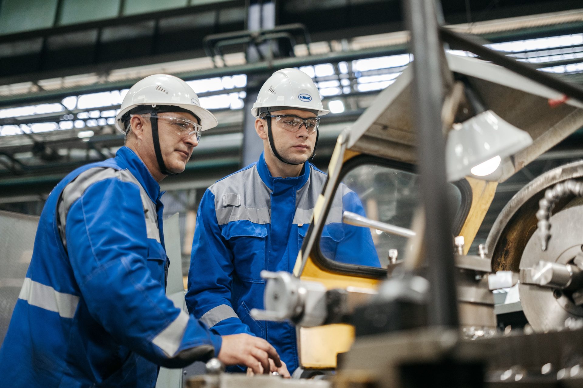 Two operators in hard hats monitoring a machine in a factory