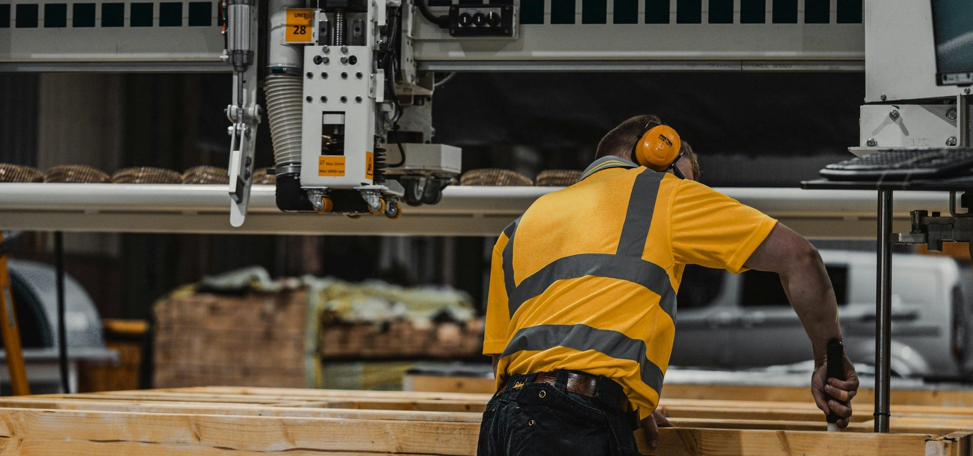 A worker in a high-visibility vest operating a woodworking machine in a workshop